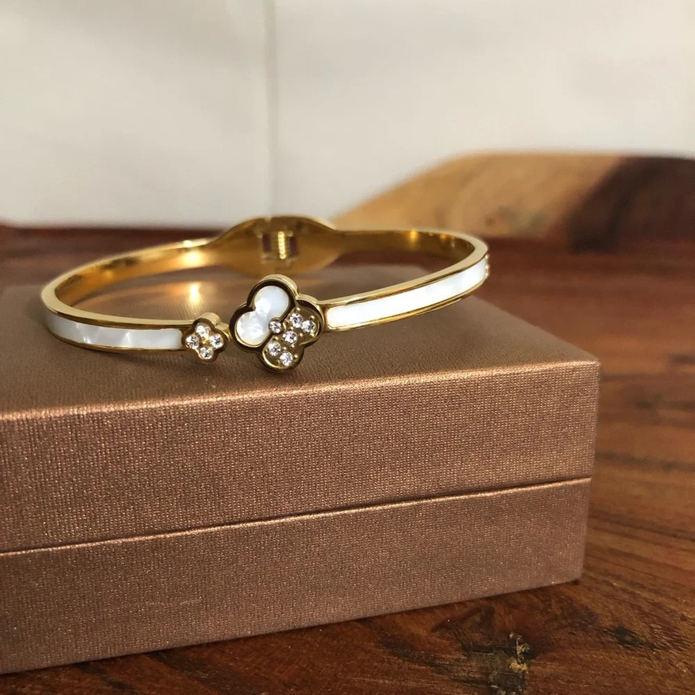gold-toned hinged bangle bracelet featuring white clover motifs and crystal New